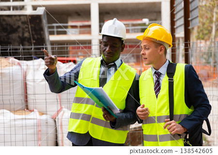 African-american engineer discussing a construction plan with a colleague shows him something African-american engineer discussing a construction plan with a colleague shows him something 138542605