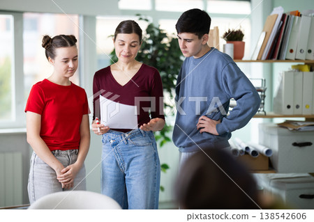 Female teacher holds papers in her hands and gives a task to schoolchildren Female teacher holds papers in her hands and gives a task to schoolchildren 138542606