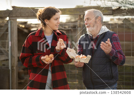 Mature man and young woman holding fresh eggs in chicken coop Mature man and young woman holding fresh eggs in chicken coop 138542608