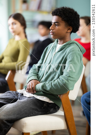 Teenage boy listening to teacher while sitting with classmates in classroom Teenage boy listening to teacher while sitting with classmates in classroom 138542611