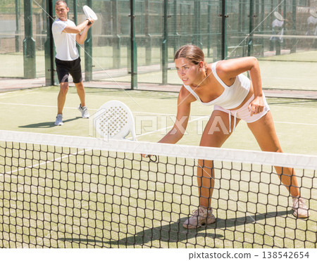 Active woman and man tennis players with rackets playing padel on an court Active woman and man tennis players with rackets playing padel on an court 138542654