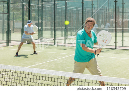 Padel game - man with partners plays on court 138542709