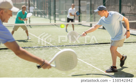 Adult and elderly men playing padel against two men Adult and elderly men playing padel against two men 138542842