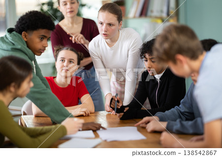Teenage students solving problem on paper while teacher watches behind Teenage students solving problem on paper while teacher watches behind 138542867