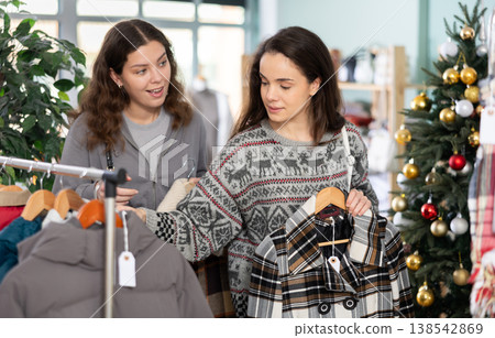 Two women choosing outerwear in a store against the background of a Christmas tree Two women choosing outerwear in a store against the background of a Christmas tree 138542869