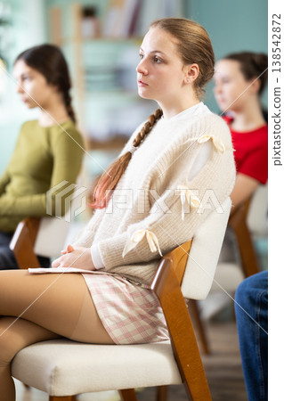 Teenage girl listening to teacher while sitting with classmates in classroom Teenage girl listening to teacher while sitting with classmates in classroom 138542872