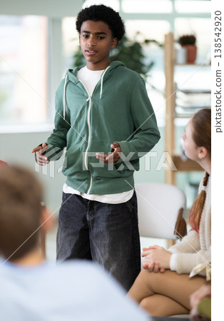 Teenage boy talking to students sitting in circle while teacher watching 138542920