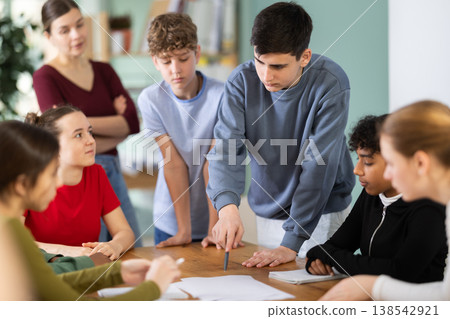 Teenage students solving problem on paper while teacher watches behind Teenage students solving problem on paper while teacher watches behind 138542921