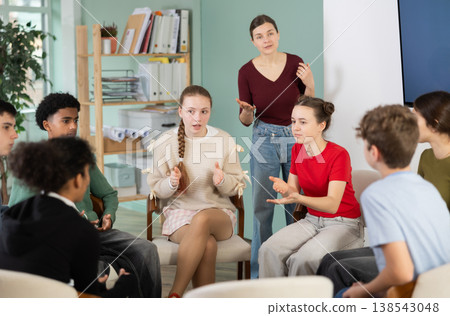 Teenage students sitting in circle and talking under supervision of teacher 138543048
