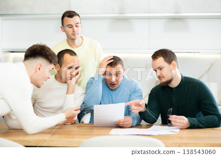 Friends reading financial documents and trying to solve problems together while sitting at table in their kitchen Friends reading financial documents and trying to solve problems together while sitting at table in their kitchen 138543060