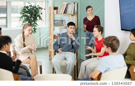 Teen pupils gathering in circle, participate at speaking club with coach, teacher watching. Teen pupils gathering in circle, participate at speaking club with coach, teacher watching. 138543087