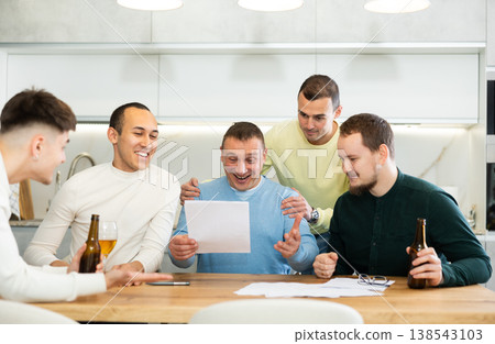 Happy friends drinking beer after solving their financial problems while sitting together at home cooking table 138543103