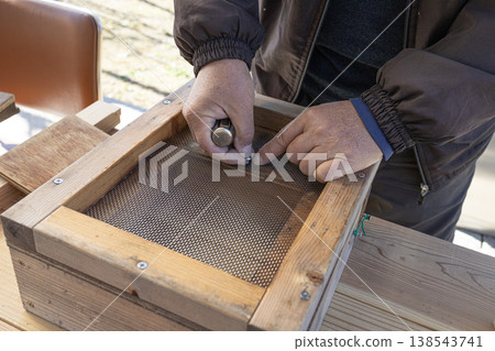 A beekeeper carefully repairs a beehive outdoors. 138543741