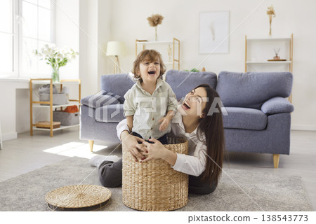 Happy mother and child playing at home with wicker basket on living room floor 138543773