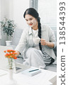 Asian woman using laptop while holding coffee cup on sofa at home, showing remote work, online browsing, digital productivity and cozy home office lifestyle in bright interior. 138544393