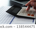 Business financial calculations and analysis. Accounting management and budget planning. Close-up of a businessman's hand using a calculator on a financial report. 138544475