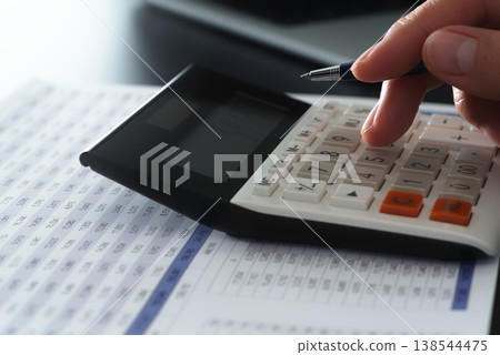 Business financial calculations and analysis. Accounting management and budget planning. Close-up of a businessman's hand using a calculator on a financial report. 138544475
