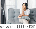 Sad woman sitting alone on sofa, hugging pillow and staring out window at home. Mental health depression, anxiety, loneliness and burnout concept for therapy, counseling and awareness with copy space. 138544505