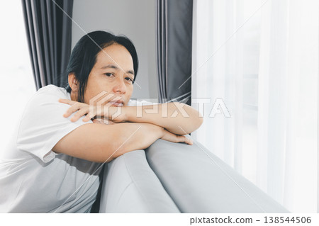 Sad woman leaning on sofa by bright window at home, feeling depressed and anxious. Mental health, loneliness and burnout concept for therapy, counseling, support and awareness campaigns, copy space. Sad woman leaning on sofa by bright window at home, feeling depressed and anxious. Mental health, loneliness and burnout concept for therapy, counseling, support and awareness campaigns, copy space. 138544506