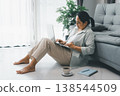 Woman working from home on laptop beside sofa, remote work setup with coffee and notebook in bright living room with copy space. Telecommuting, freelance home office productivity concept. 138544509