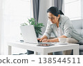 Woman working from home at coffee table on laptop, focused in bright living room with tablet and cup. Remote work and home office productivity for telecommuting and freelance. remote, work, office 138544511