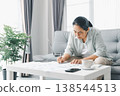 Woman working from home on sofa, writing notes on business charts at coffee table with laptop, smartphone and cup in bright living room. Remote work productivity. Home office planning and analysis. 138544513