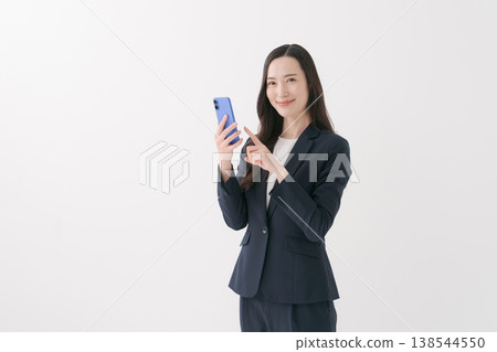 A woman in a suit smiles while looking at her smartphone. A woman in a suit smiles while looking at her smartphone. 138544550