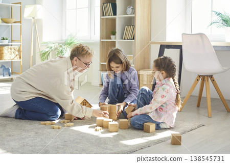 Grandmother and two children playing with wooden blocks, building tower during leisure at home. Grandmother and two children playing with wooden blocks, building tower during leisure at home. 138545731