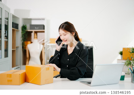 Asian online seller talking on the phone with a customer while managing orders on her laptop. Modern ecommerce, small business Asian online seller talking on the phone with a customer while managing orders on her laptop. Modern ecommerce, small business 138546195