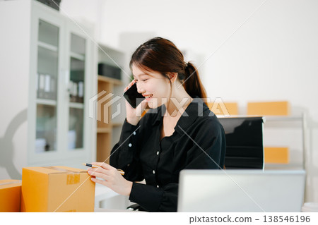 Asian online seller talking on the phone with a customer while managing orders on her laptop. Modern ecommerce, small business 138546196