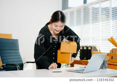Entrepreneurial Asian woman prepares parcels and checks online orders on tablet and laptop for delivery online shopping and small business success in office Entrepreneurial Asian woman prepares parcels and checks online orders on tablet and laptop for delivery online shopping and small business success in office 138546302