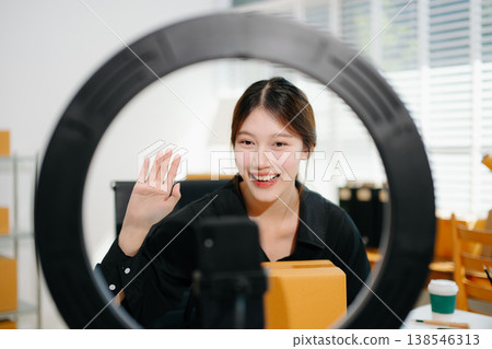 Beautiful Asian lady blogger showing clothes in front of the camera to recording vlog video live streaming at her shop. Online Shopping Cart notion. Beautiful Asian lady blogger showing clothes in front of the camera to recording vlog video live streaming at her shop. Online Shopping Cart notion. 138546313