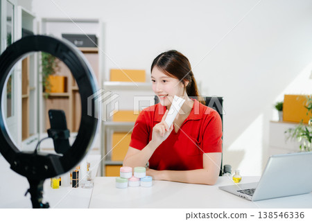 Asian beauty influencer filming skincare review with ring light, showcasing cosmetic jars and products for online content, beauty marketing, and social media promotions. 138546336
