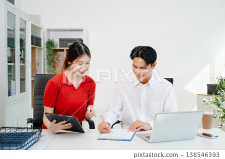 Two Asian coworkers collaborating on business planning, discussing documents and using digital devices in modern office Two Asian coworkers collaborating on business planning, discussing documents and using digital devices in modern office 138546393