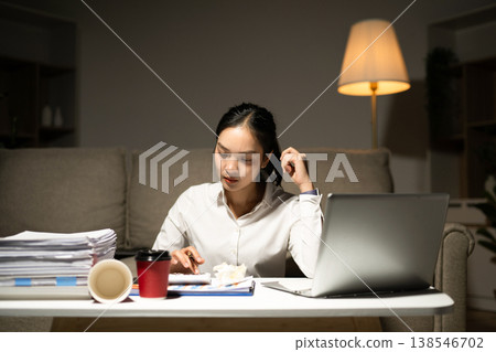 Stressed businesswoman working late at home with laptop and paperwork. Deadline pressure, overtime, workload, finance and modern business lifestyle concept. Stressed businesswoman working late at home with laptop and paperwork. Deadline pressure, overtime, workload, finance and modern business lifestyle concept. 138546702