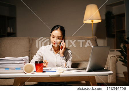Stressed businesswoman talking on phone while working late with laptop and paperwork. Deadline pressure, finance problems, overtime 138546706