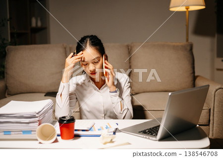 Stressed businesswoman talking on phone while working late with laptop and paperwork. Deadline pressure, finance problems, overtime Stressed businesswoman talking on phone while working late with laptop and paperwork. Deadline pressure, finance problems, overtime 138546708