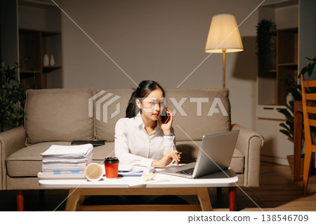Stressed businesswoman talking on phone while working late with laptop and paperwork. Deadline pressure, finance problems, overtime Stressed businesswoman talking on phone while working late with laptop and paperwork. Deadline pressure, finance problems, overtime 138546709
