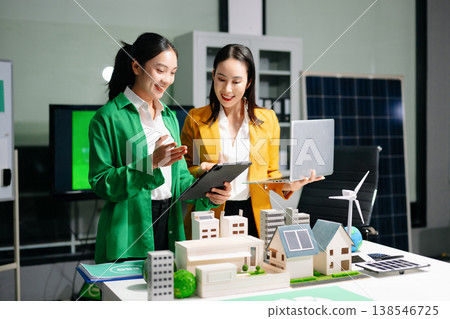 Businesswomen discussing net zero sustainability strategy with renewable energy models, solar panels and green office concepts, representing eco friendly business 138546725