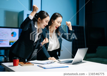 Two businesswomen celebrating success after achieving goals at office desk. Teamwork, motivation, leadership, startup growth and modern corporate workplace. Two businesswomen celebrating success after achieving goals at office desk. Teamwork, motivation, leadership, startup growth and modern corporate workplace. 138546775