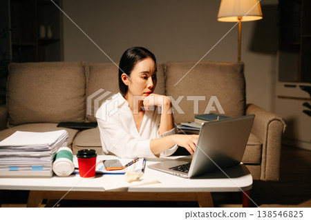 Stressed Asian woman using calculator and laptop for financial accounting and tax report late at night at home. Stressed Asian woman using calculator and laptop for financial accounting and tax report late at night at home. 138546825