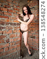 Young woman in bikini smiling and peeking through brick wall opening, playful summer concept 138548274