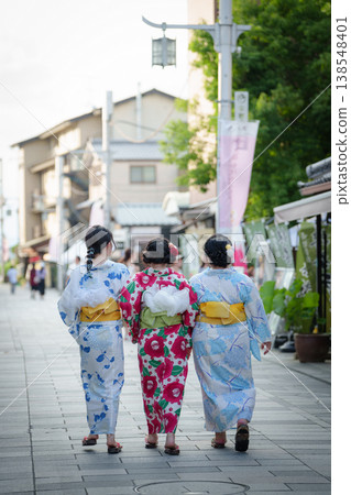 The backs of three women in yukata (summer kimonos) walking together along the approach to Byodo-in Temple. Uji City, Kyoto Prefecture, Japan. The backs of three women in yukata (summer kimonos) walking together along the approach to Byodo-in Temple. Uji City, Kyoto Prefecture, Japan. 138548401