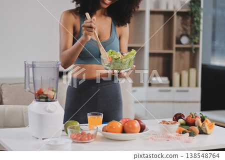 Young nutritionist showing bell peppers during an online video call consulting about healthy eating, sitting at home at a table with vegetables, laptop and measuring tape 138548764