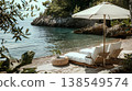 lifestyle photography, beach lounge with white linen and wicker furniture on the shore of a mediterranean cove where there is an umbrella to shading from the sun 138549574
