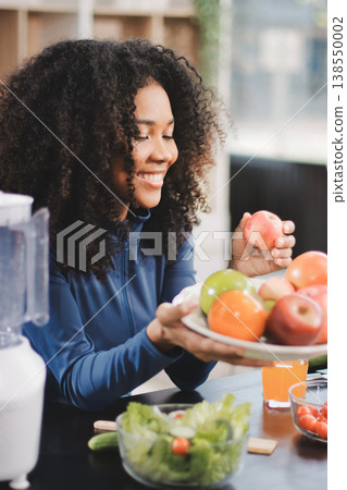 Young nutritionist showing bell peppers during an online video call consulting about healthy eating, sitting at home at a table with vegetables, laptop and measuring tape 138550002