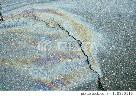 Iridescent oil dispersing on wet asphalt, showing colorful patterns and a prominent crack on the road surface after rain 138550116