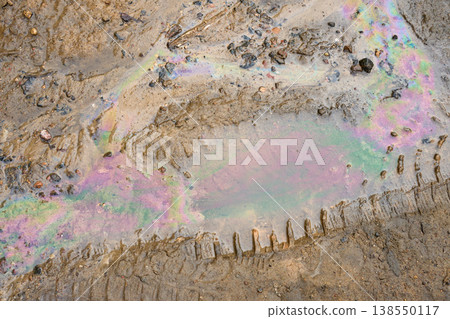 Iridescent liquid layer creating a colorful, captivating pattern on a muddy puddle, reflecting light and displaying environmental impact 138550117