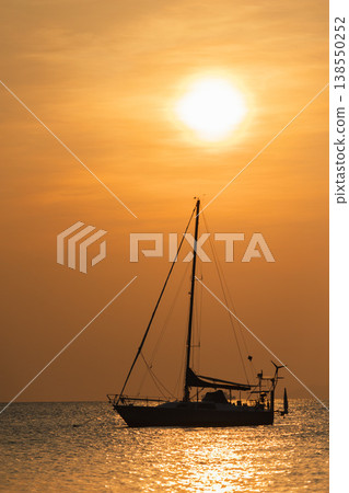 Sailing yacht silhouette anchored on calm sea at golden sunset with bright sun above horizon and shimmering water reflections Sailing yacht silhouette anchored on calm sea at golden sunset with bright sun above horizon and shimmering water reflections 138550252