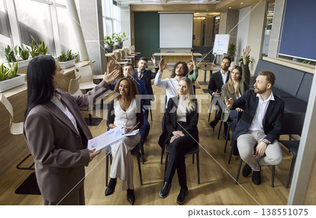 Corporate team seminar with speaker and employees raising hands during training Corporate team seminar with speaker and employees raising hands during training 138551075